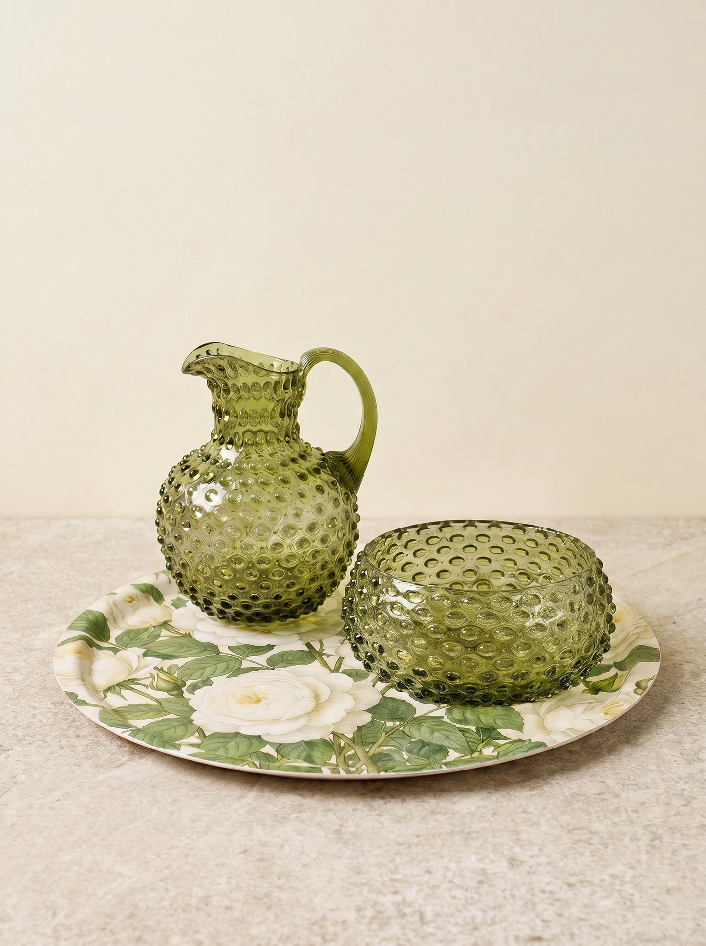 Green glass pitcher and bowl on a decorative plate with floral pattern