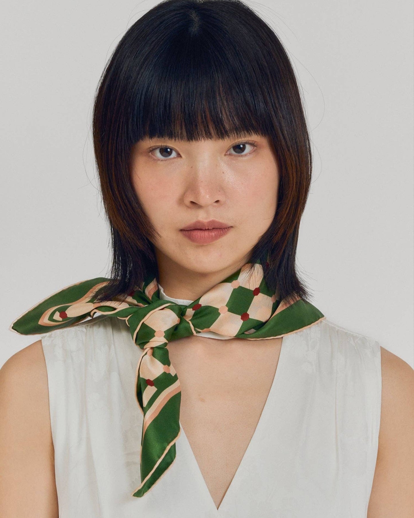 Woman wearing a green and beige patterned scarf on a plain background