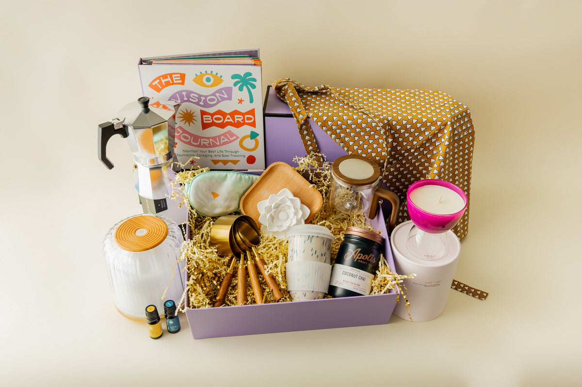 Gift basket with various items including a book, candles, and a teapot on a light background