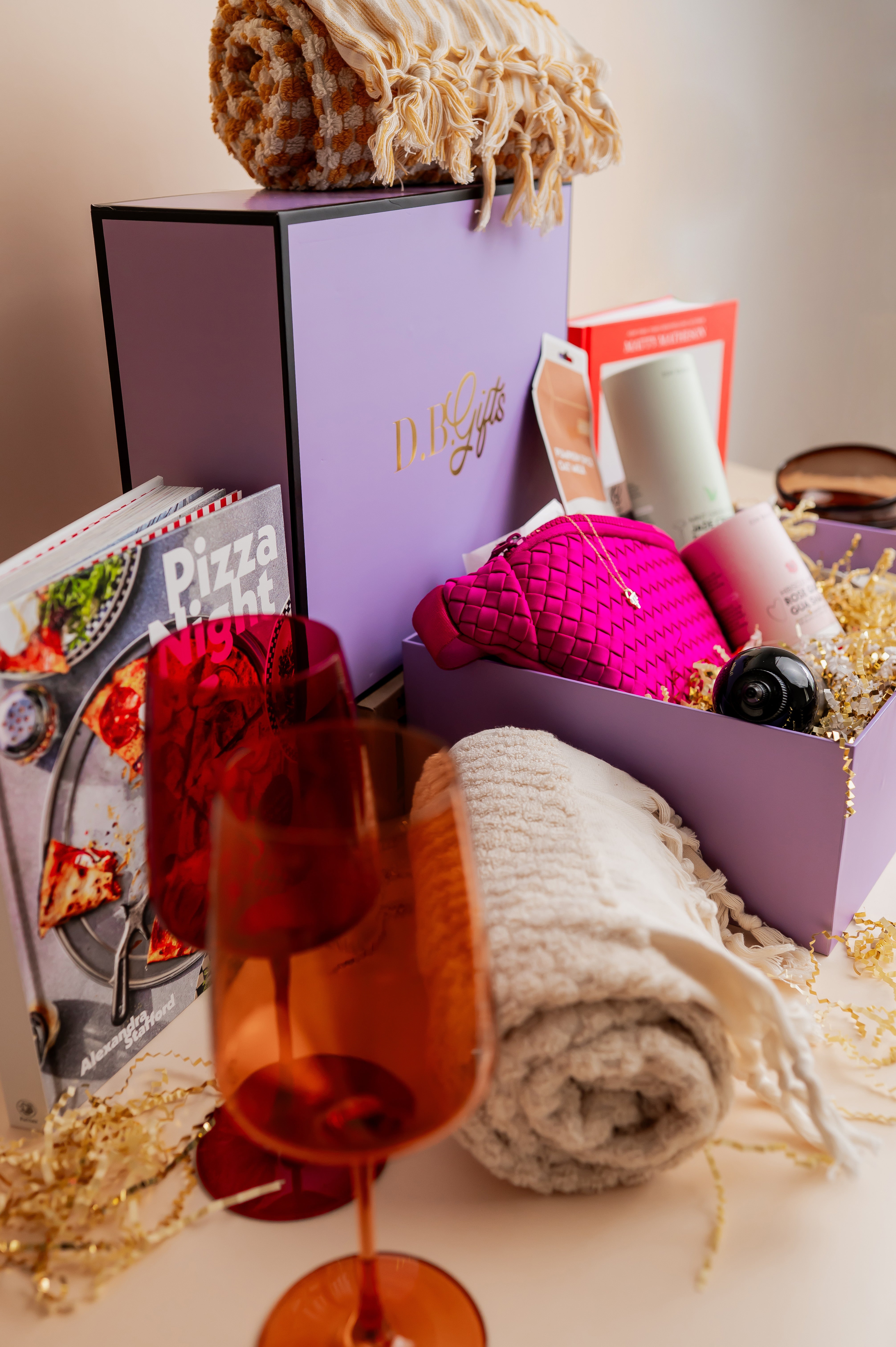 Gift box with pizza-themed book, wine, and blankets on a table