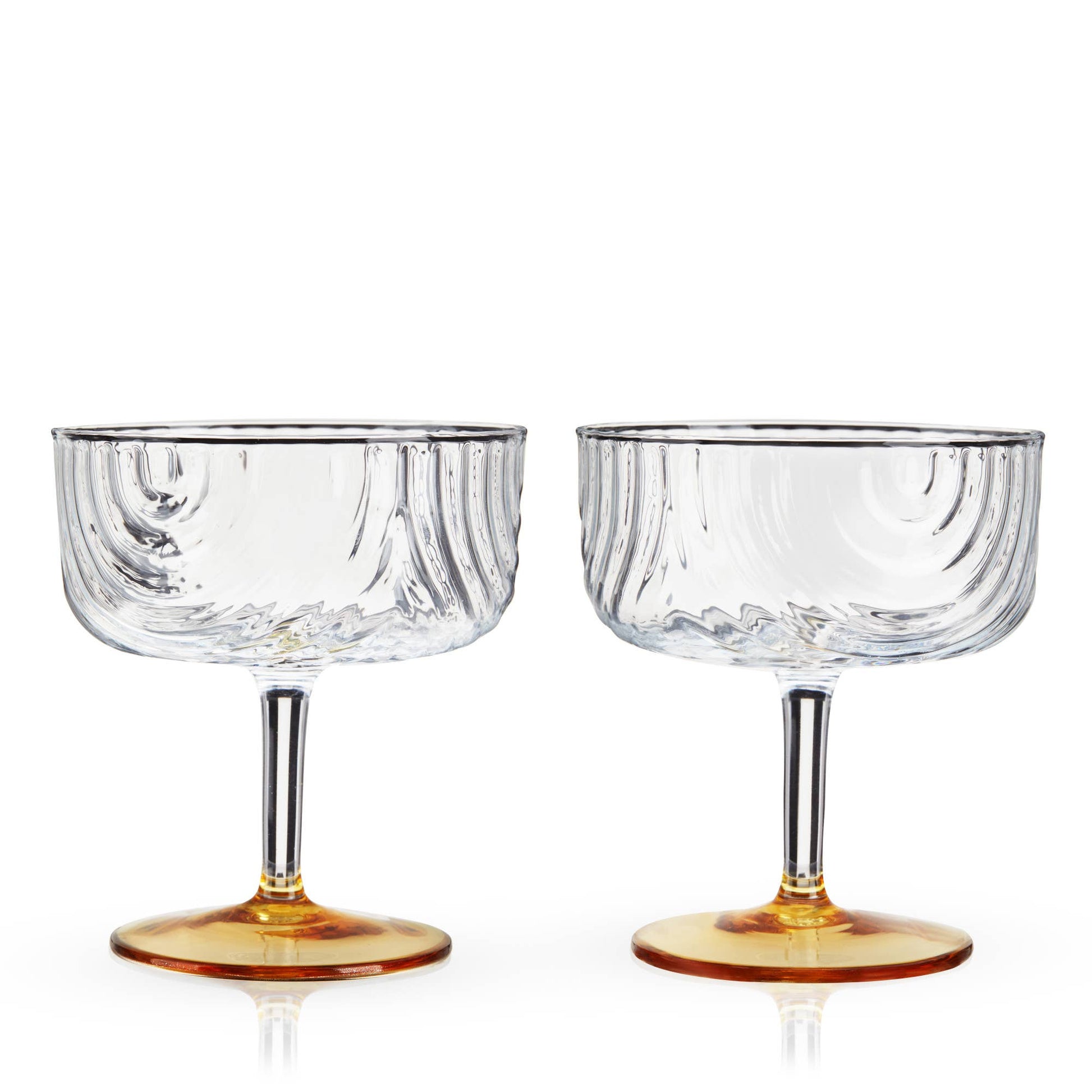 Two clear glass coupe glasses with amber bases on a white background