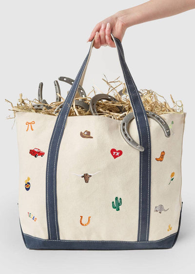 Tote bag with embroidered designs held by a hand on a white background