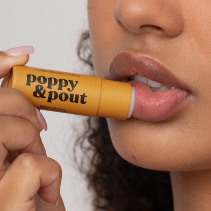Person applying a lip balm labeled 'Poppy & Pout' to their lips.